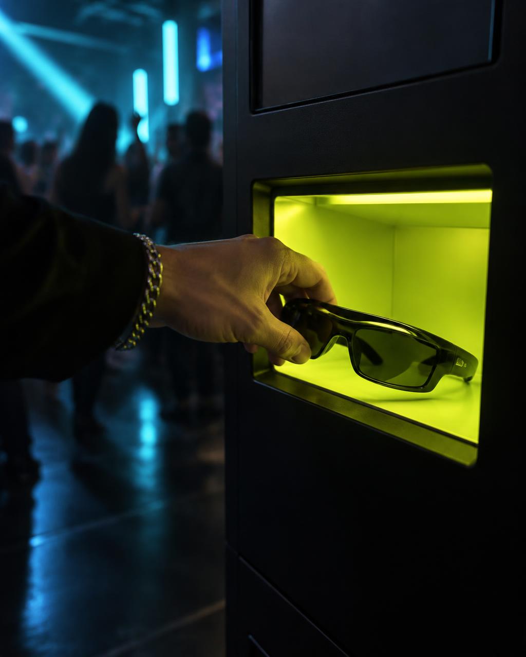 A hand taking a pair of sunglasses out of the lit dispensing niche of a vendo lol machine